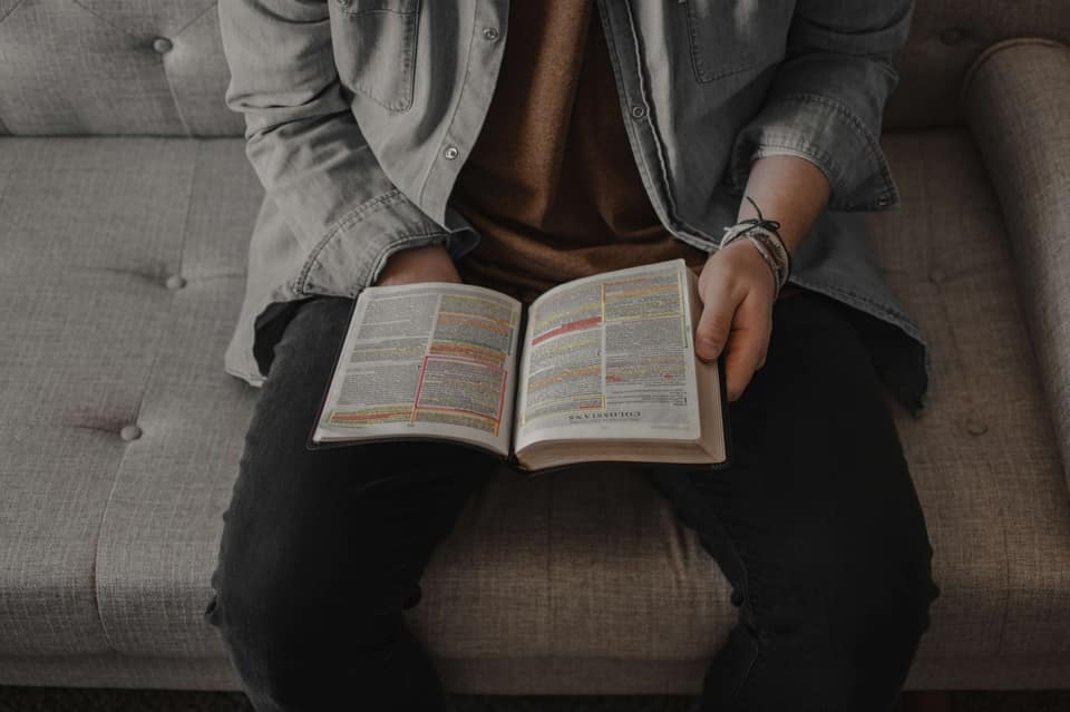 Person seated on a couch holding an open book