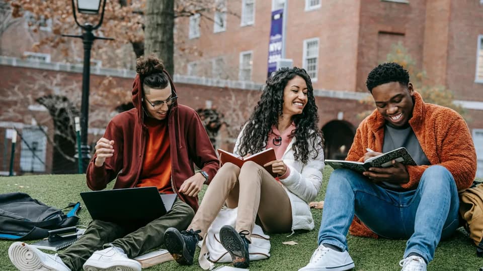 Three students sitting on grass studying together outdoors
