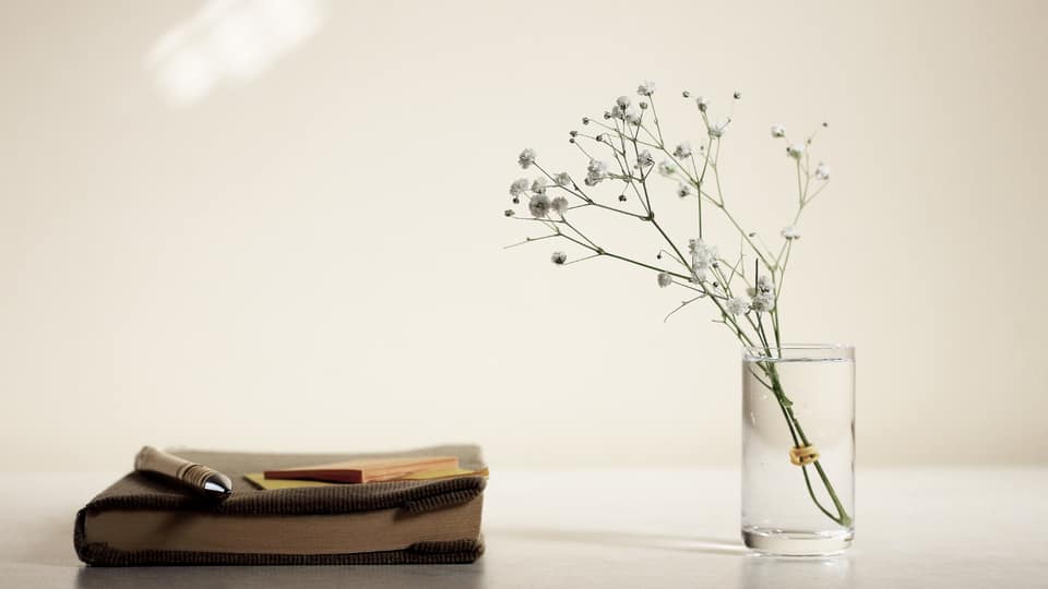 Closed book with a pen beside a glass vase of white flowers