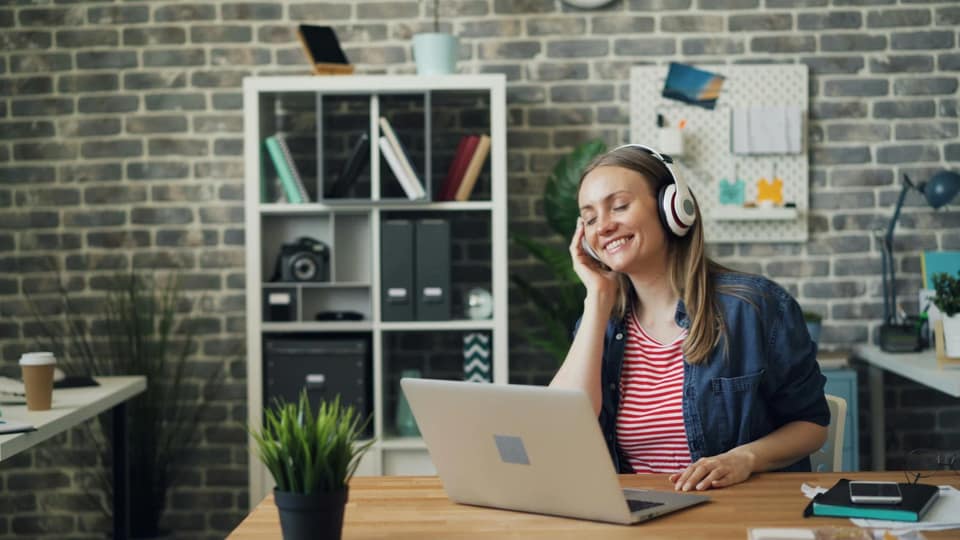 Woman wearing headphones and smiling at a laptop in an office